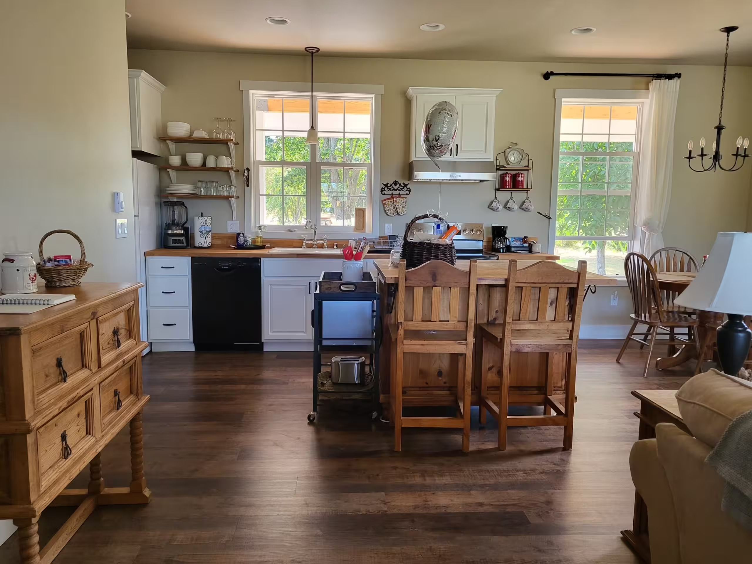 A kitchen with wooden cabinets, a central island with chairs, a dining table, and a view through large windows.