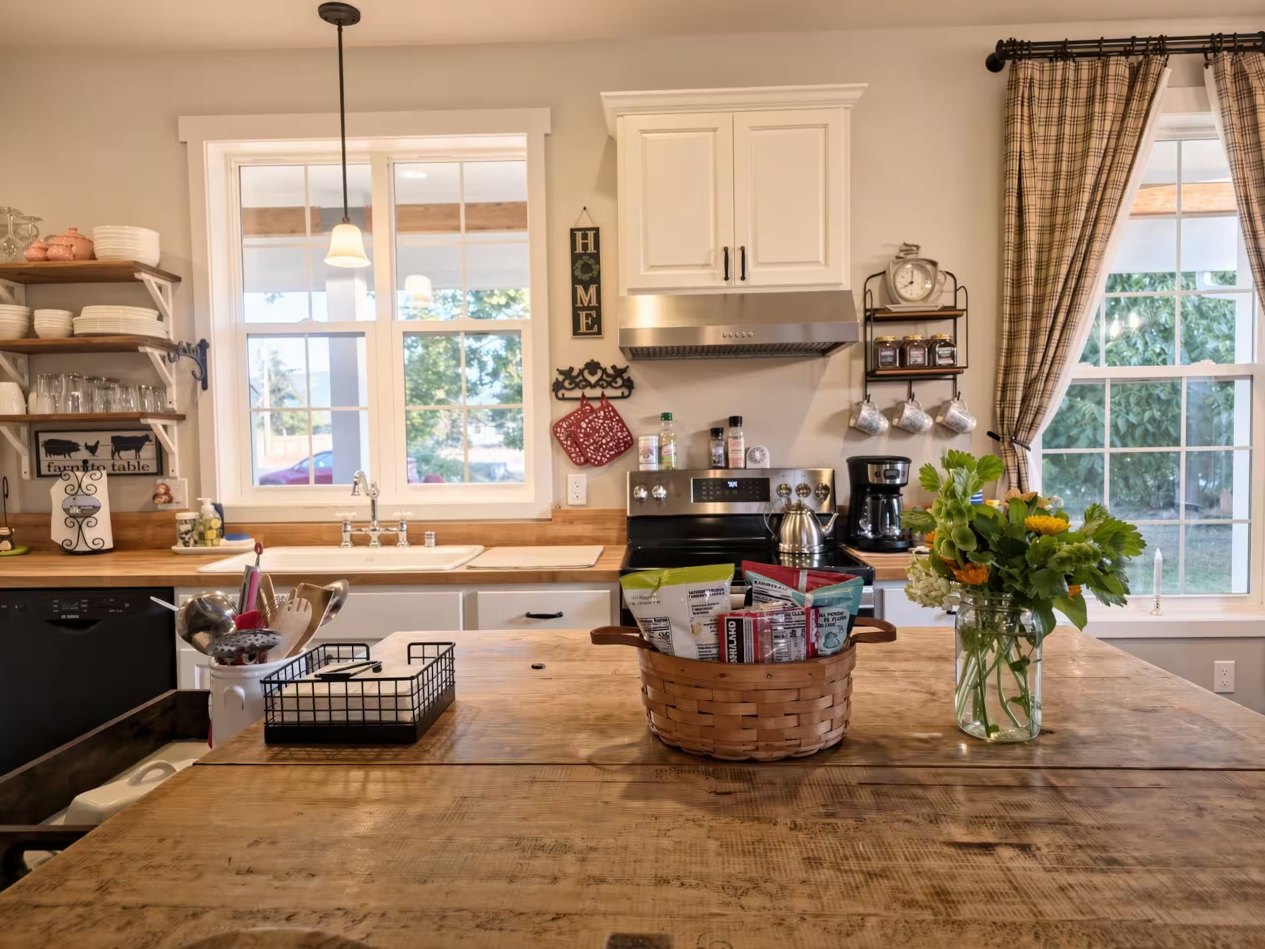 A kitchen with white cabinets, a stove, a coffee maker, and a window with curtains.