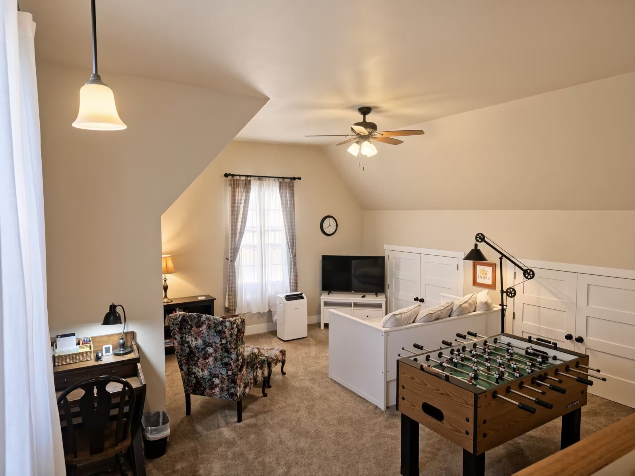 A cozy room with a foosball table, a TV, a sofa, and a desk with a lamp.