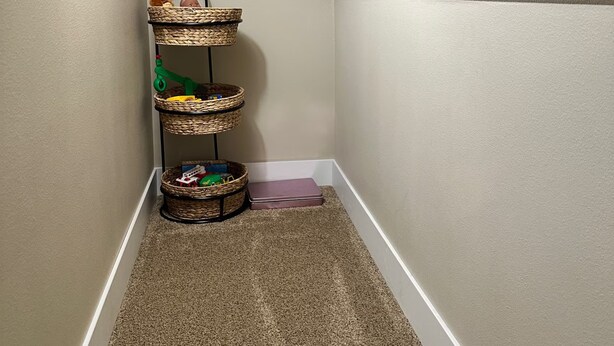 Canto de um quarto com piso coberto por carpete, parede com acabamento texturizado e prateleira embutida com cestos.