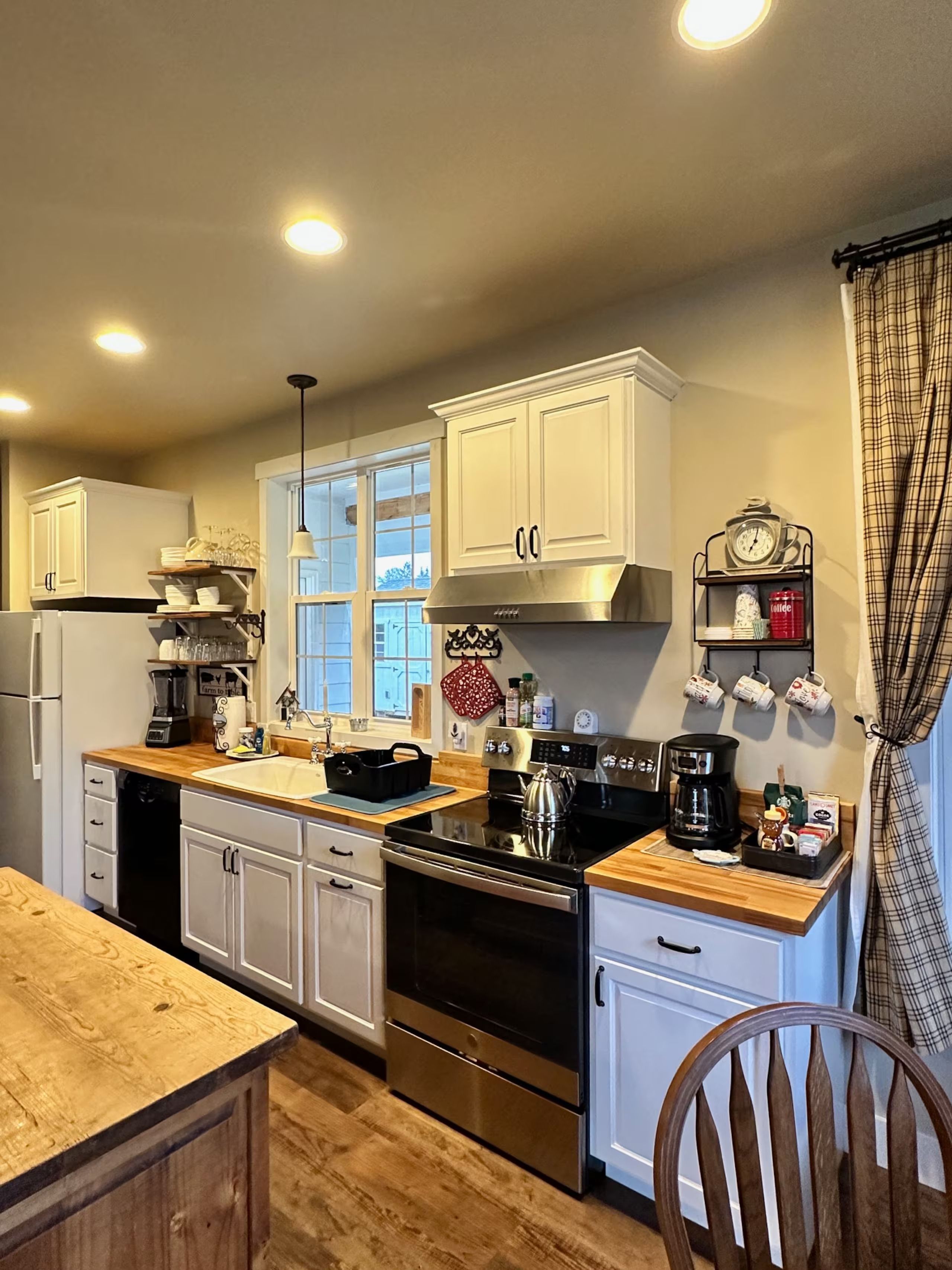 Una cocina con armarios blancos, estufa de acero inoxidable y encimera de madera.