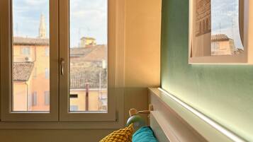 A bedroom with a bed, two pillows, a window, and a view of buildings outside.