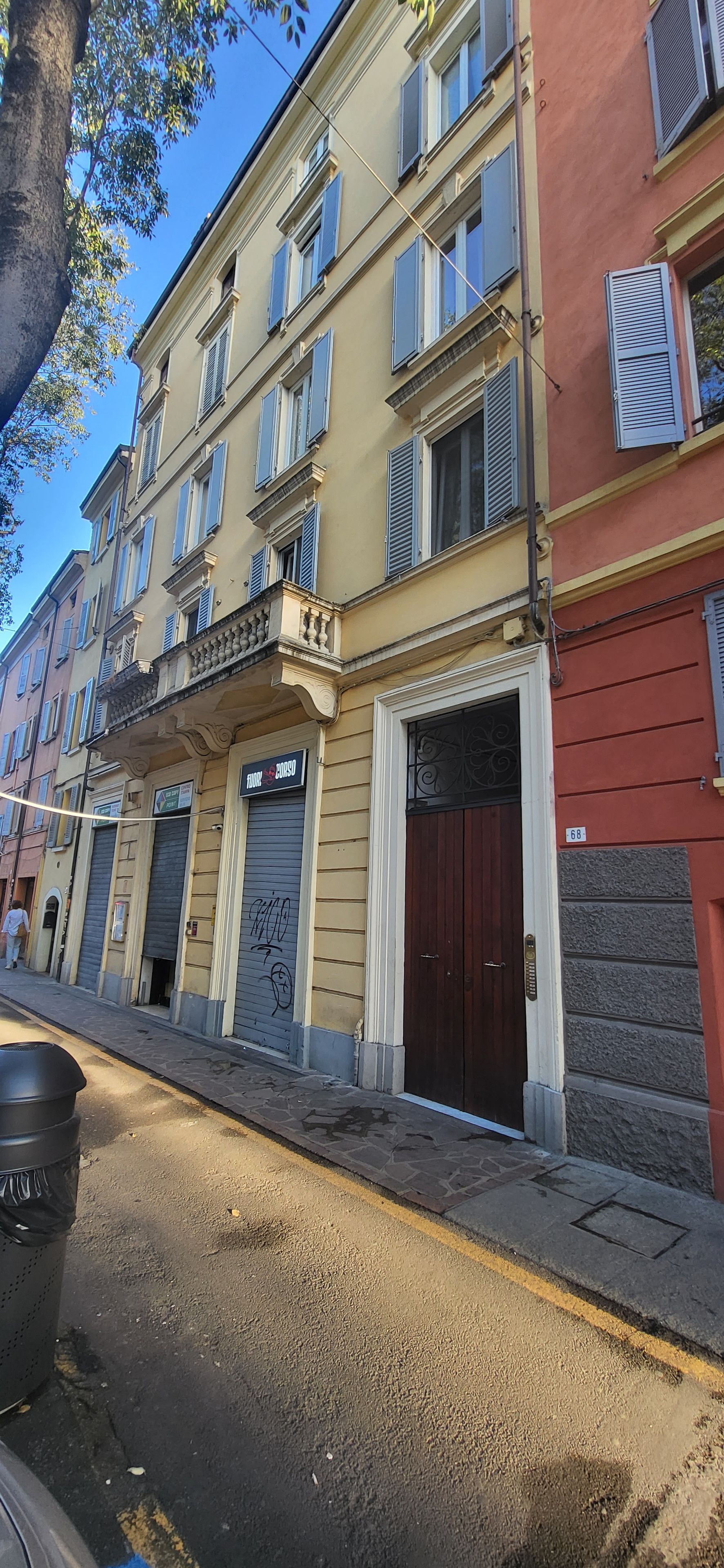 A multi-story building with a ground-floor shop, closed shutters, and a dark brown door.