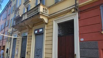 A multi-story building with a ground-floor shop, closed shutters, and a dark brown door.