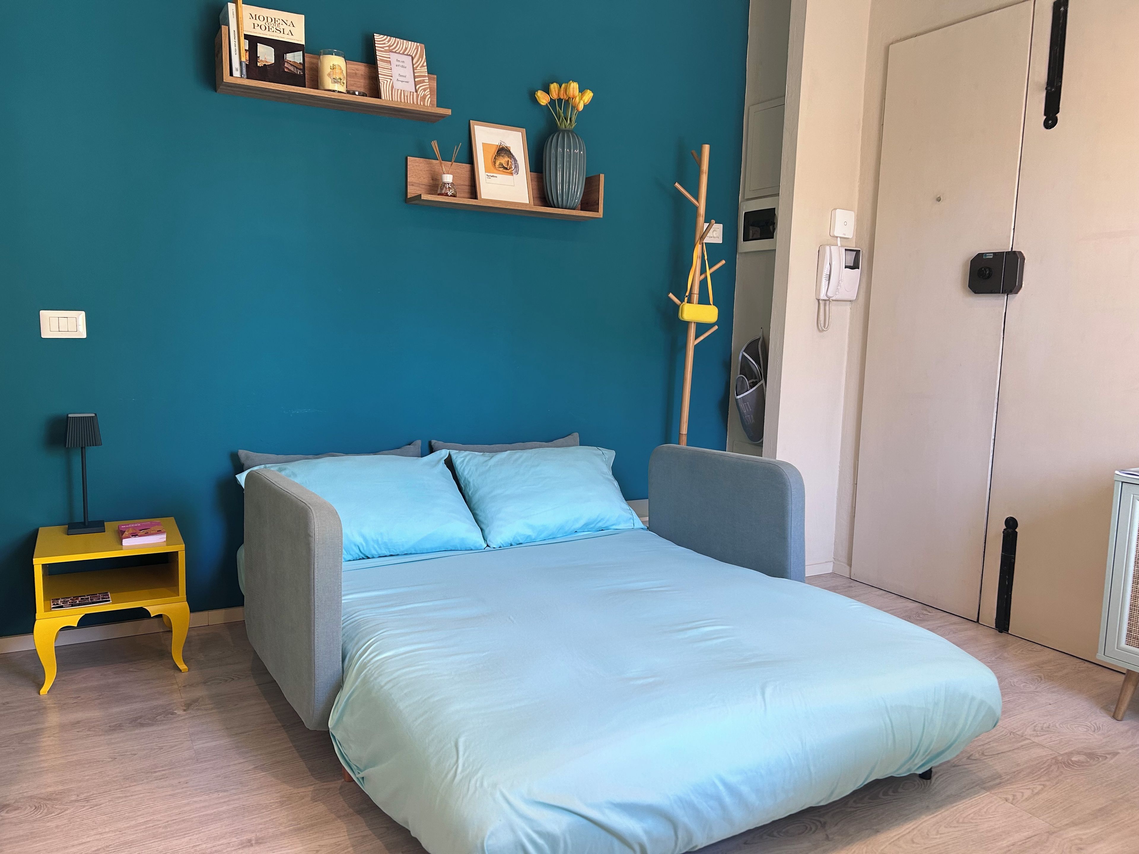 Une chambre à coucher avec un lit, une table de chevet avec une lampe et une étagère murale avec des livres et un vase.