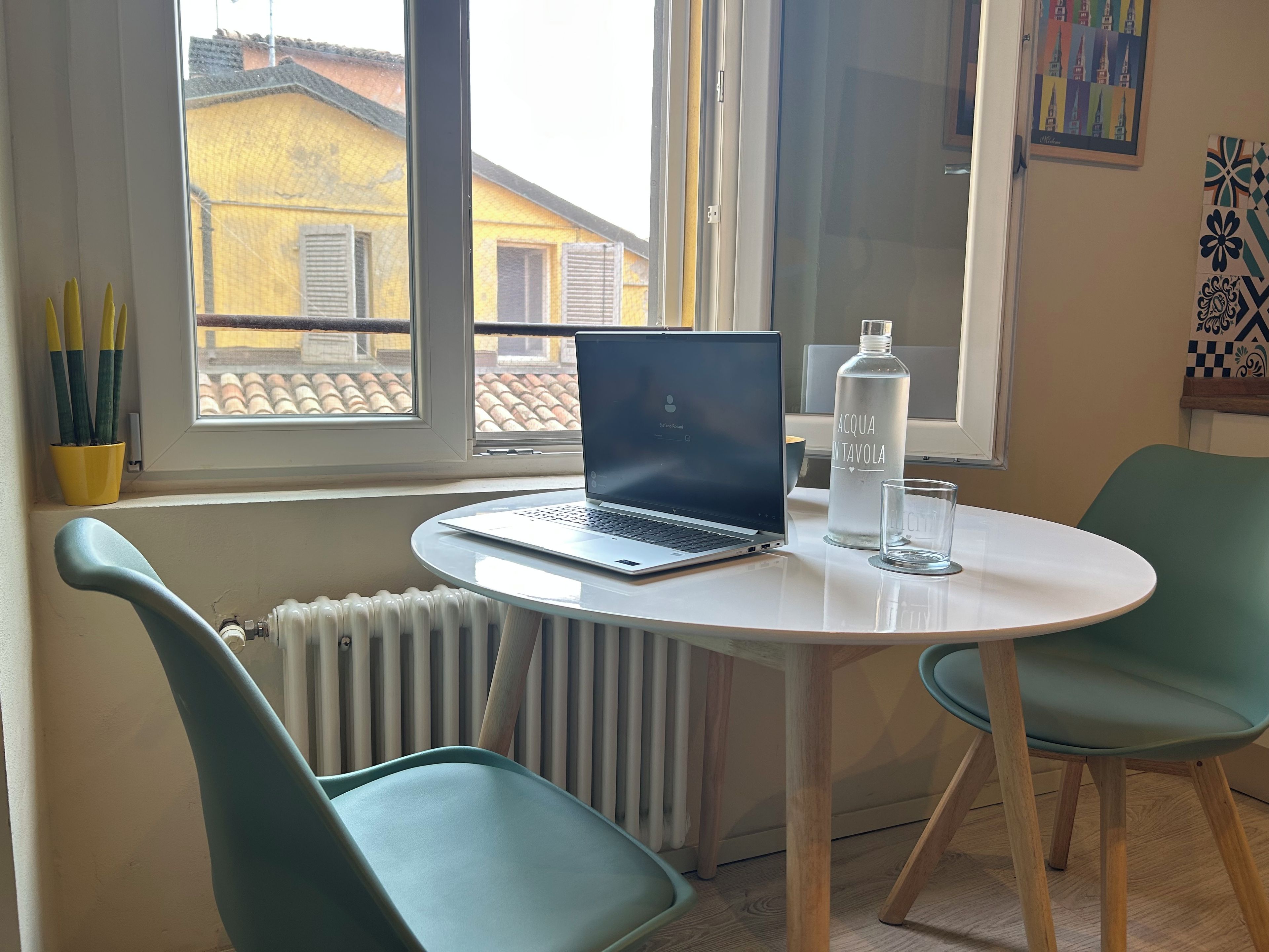 Une pièce avec un ordinateur portable posé sur une table ronde, une bouteille d’eau et un verre. Il y a deux chaises et un radiateur.
