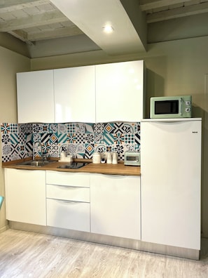Una cocina con armarios blancos, un salpicadero estampado, un microondas encima de un refrigerador blanco y una encimera de madera.