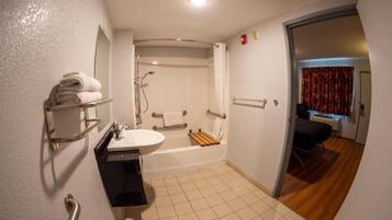 Une salle de bain équipée d’un lavabo, d’un miroir, d’un porte-serviettes, d’une douche et d’une porte donnant sur une chambre.