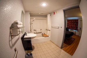 Un baño con lavamanos, espejo, toallero, ducha y una puerta que da a un dormitorio.