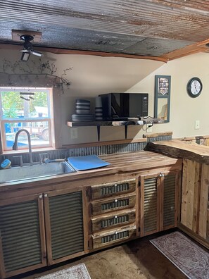 Une cuisine avec un plan de travail en bois, un évier, un four à micro-ondes et une horloge au mur.