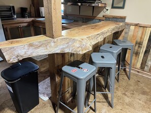 A bar area with a wooden countertop, stools, and a trash bin.