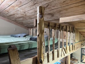 Une chambre à coucher aménagée dans les combles, avec un plafond en pente, un lit superposé et une rambarde en bois.