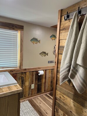 A bathroom with wooden walls, a window with blinds, a towel rack, and a toilet paper holder. - Greenlawn GetAway 2.0 Blue-Door Edition (Perry)