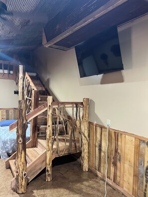 A rustic wooden staircase with a natural finish, leading to a loft area with a slanted ceiling.