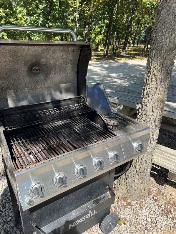 A portable grill with four burners, a handle, and a control knob, set up outdoors.