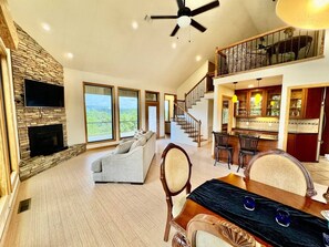 A spacious living area with a fireplace, a sofa, a dining table with chairs, and a staircase leading to an upper level. - Top of the World Hot Springs (Hot Springs)