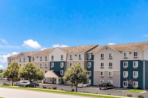 A multi-story hotel with a modern design, featuring a mix of beige and teal colors, a covered parking area, and a well-maintained lawn.