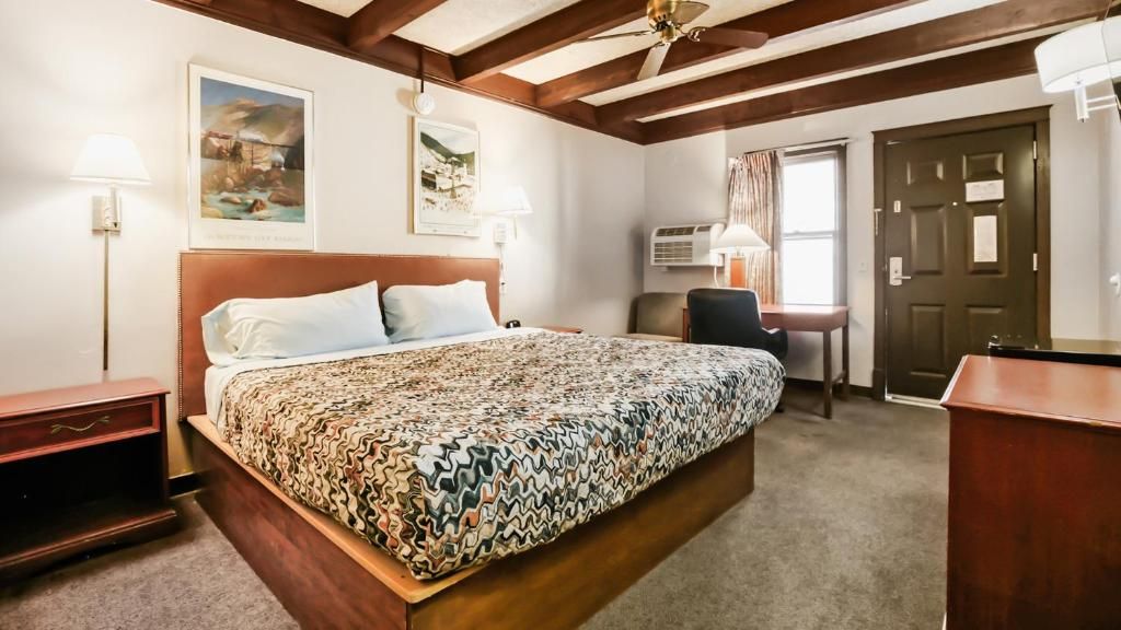A hotel room with a large bed, a desk, a chair, a wardrobe, and an air conditioning unit.