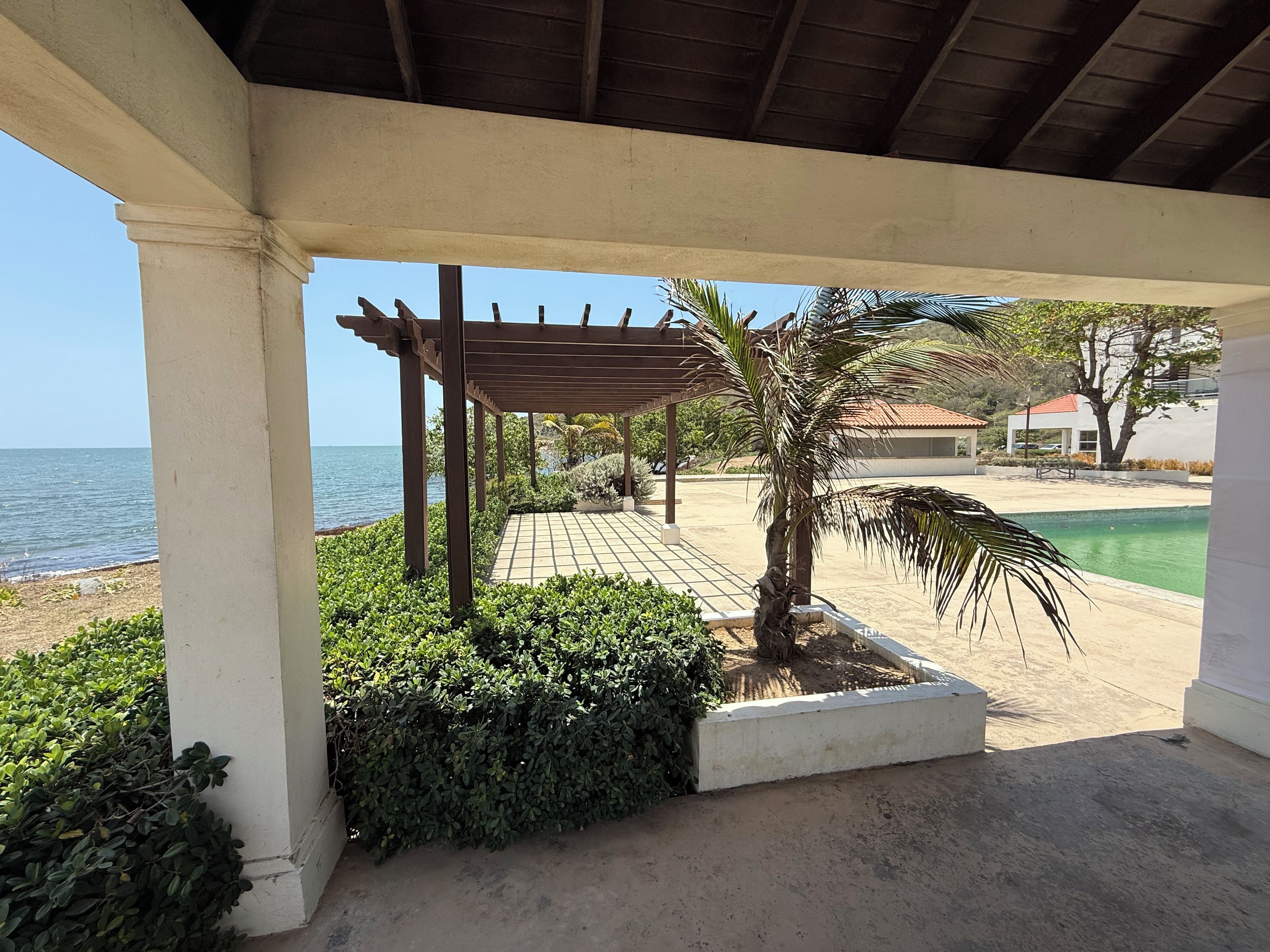 Un espacio al aire libre cubierto con un pérgola, palmeras y vista al mar.