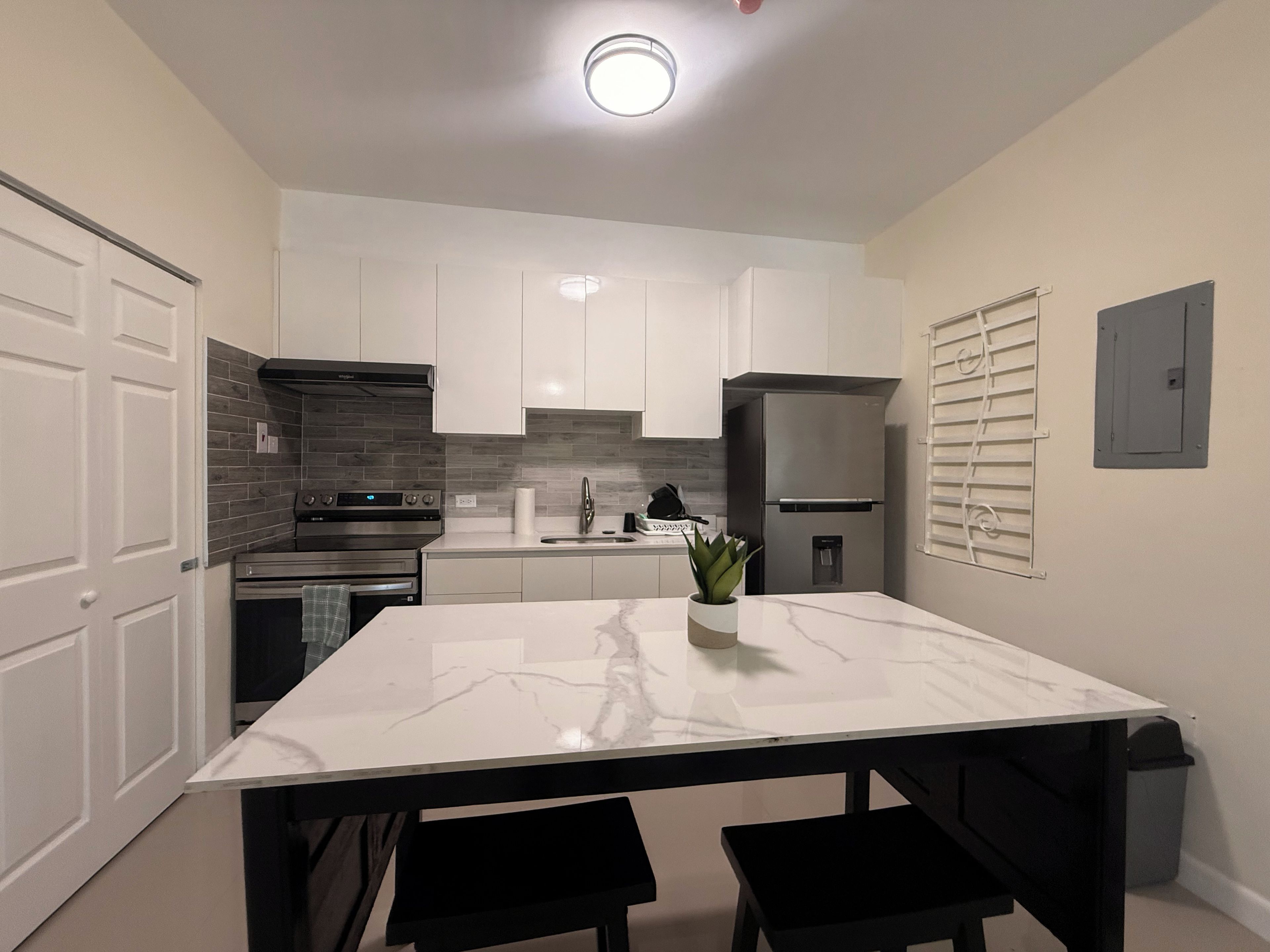 Una cocina moderna con armarios blancos, encimera de mármol y refrigerador de acero inoxidable.