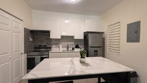 Una cocina moderna con armarios blancos, encimera de mármol y refrigerador de acero inoxidable.