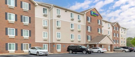 A multi-story hotel with a brick facade, multiple windows, and a parking lot with several cars.