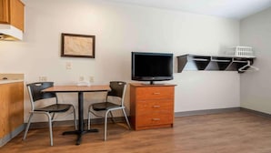 Een kleine kamer met een houten tafel, twee stoelen, een televisie op een standaard, een witte muur en een houten kast.