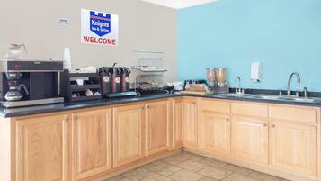 A hotel kitchen with a coffee station, a sign reading 'Knights Inn & Suites Welcome', and a blue wall.