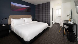 Een hotelkamer met een groot bed, een bureau, een stoel, een televisie en een schilderij aan de muur.