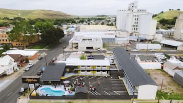 A motel with a swimming pool, parking lot, and a large industrial building in the background.