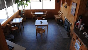 Een restaurantinterieur met houten tafels en stoelen, een betegelde vloer en een raam met zonwering.