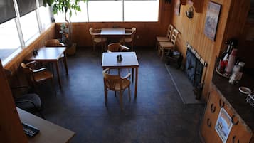 A restaurant interior with wooden tables and chairs, a tiled floor, and a window providing natural light.