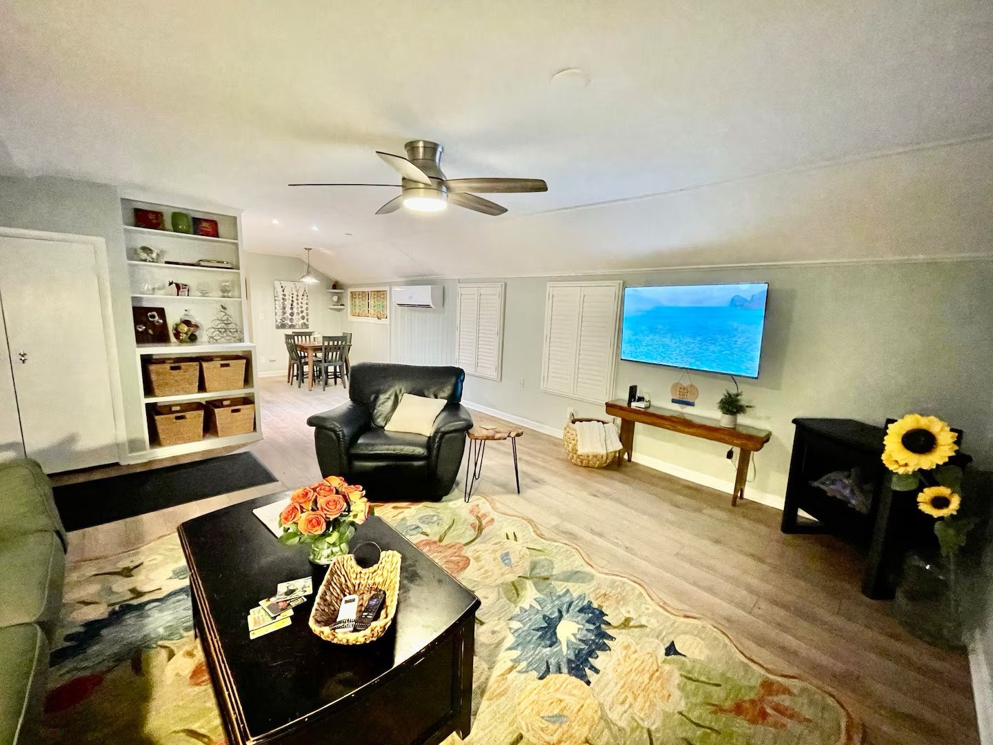 A living room with a black leather chair, a television, a ceiling fan, and a floral rug.