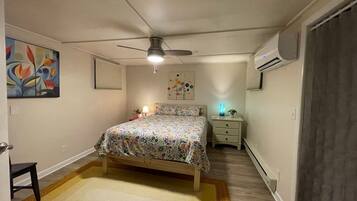 Quarto com cama, ventoinha no teto, mesa de cabeceira, abajur e um quadro na parede.