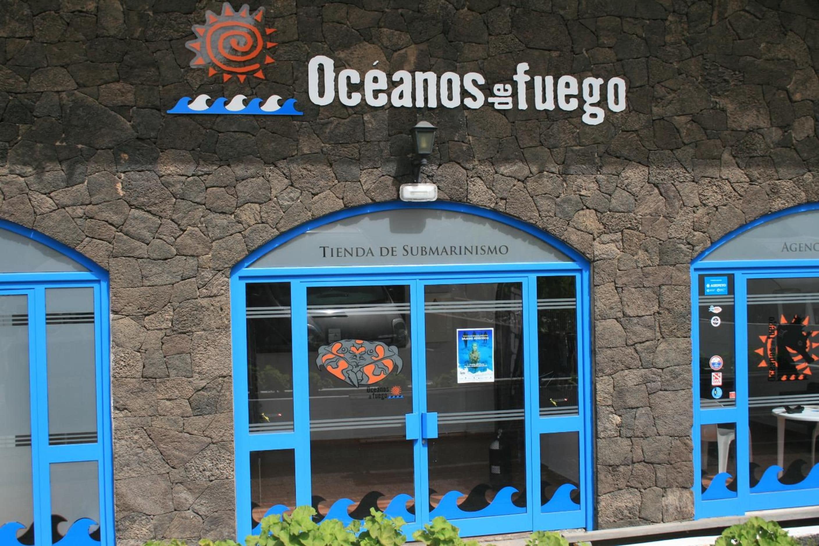 A building facade with the sign 'Oceanos de fuego' and a storefront named 'TIENDA DE SUBMARINISMO' with a poster inside.