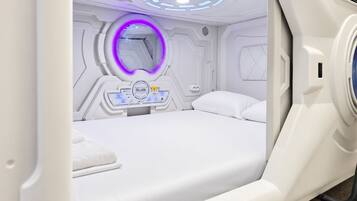 Una habitación moderna de estilo cápsula, con cama, panel de control y lámpara circular.