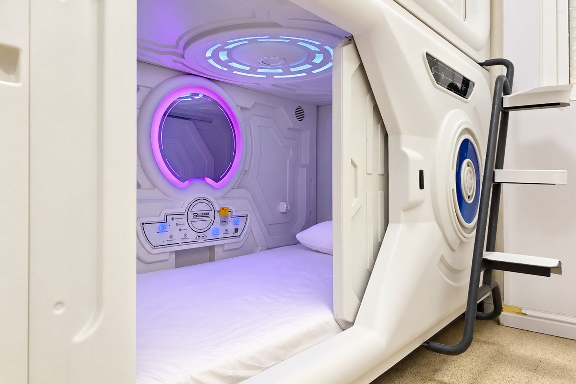 A modern, white, single-bed room with a control panel and a circular light feature.