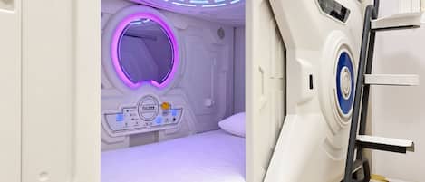 A modern, white, single-bed room with a control panel and a circular light feature.