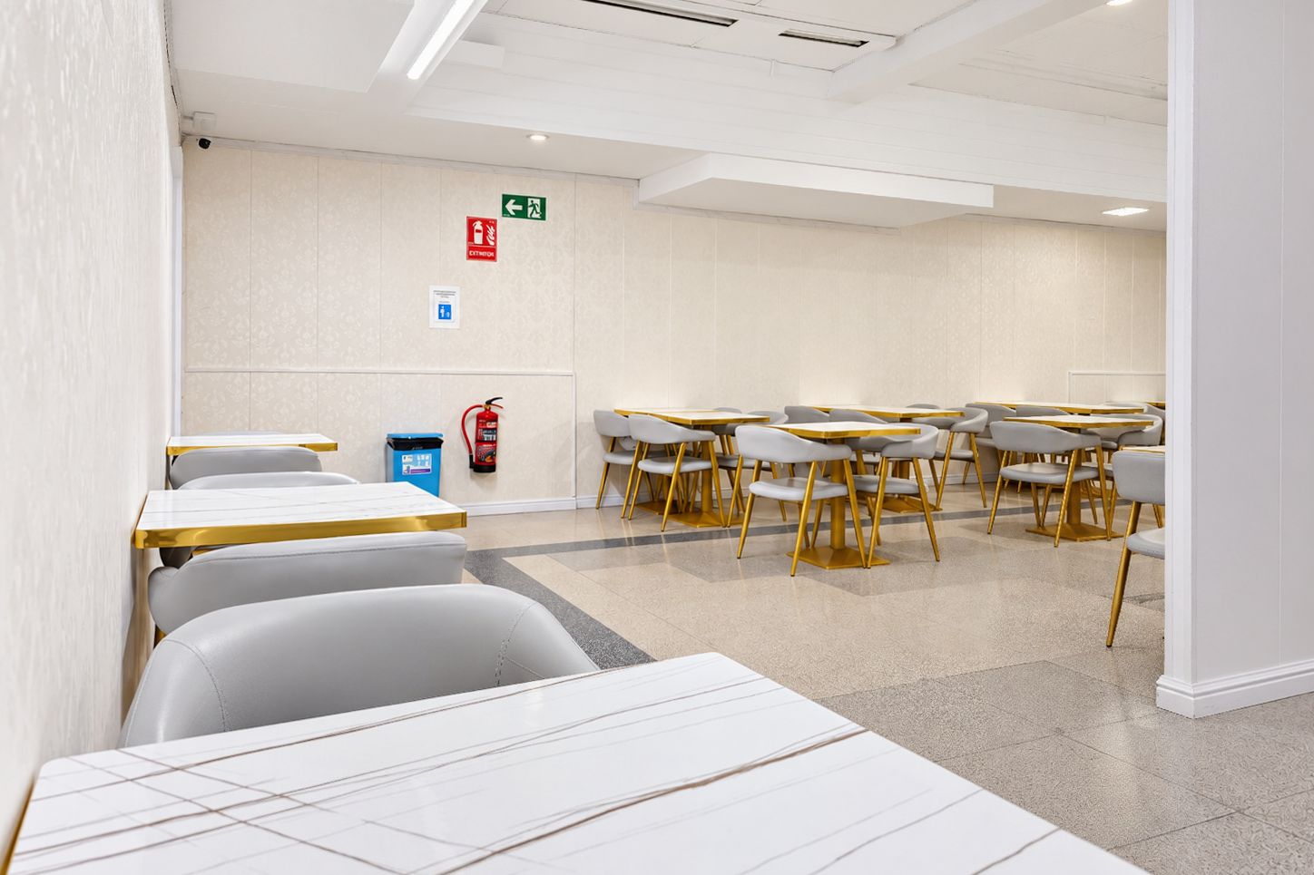 Una sala de conferencias moderna con paredes blancas, mesas y sillas con detalles dorados, y un extintor de incendios colgado en la pared.