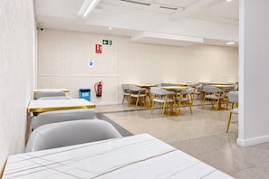 A modern conference room with white walls, gold-trimmed tables and chairs, and a fire extinguisher mounted on the wall.