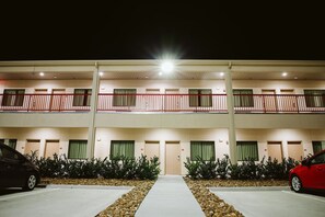 Een meerlaags hotel met een centrale gang, balkons en een parkeerplaats.
