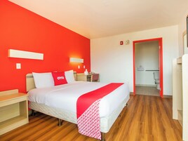 Una habitación de hotel con una cama, mesitas de noche, una pared roja y suelo de madera.