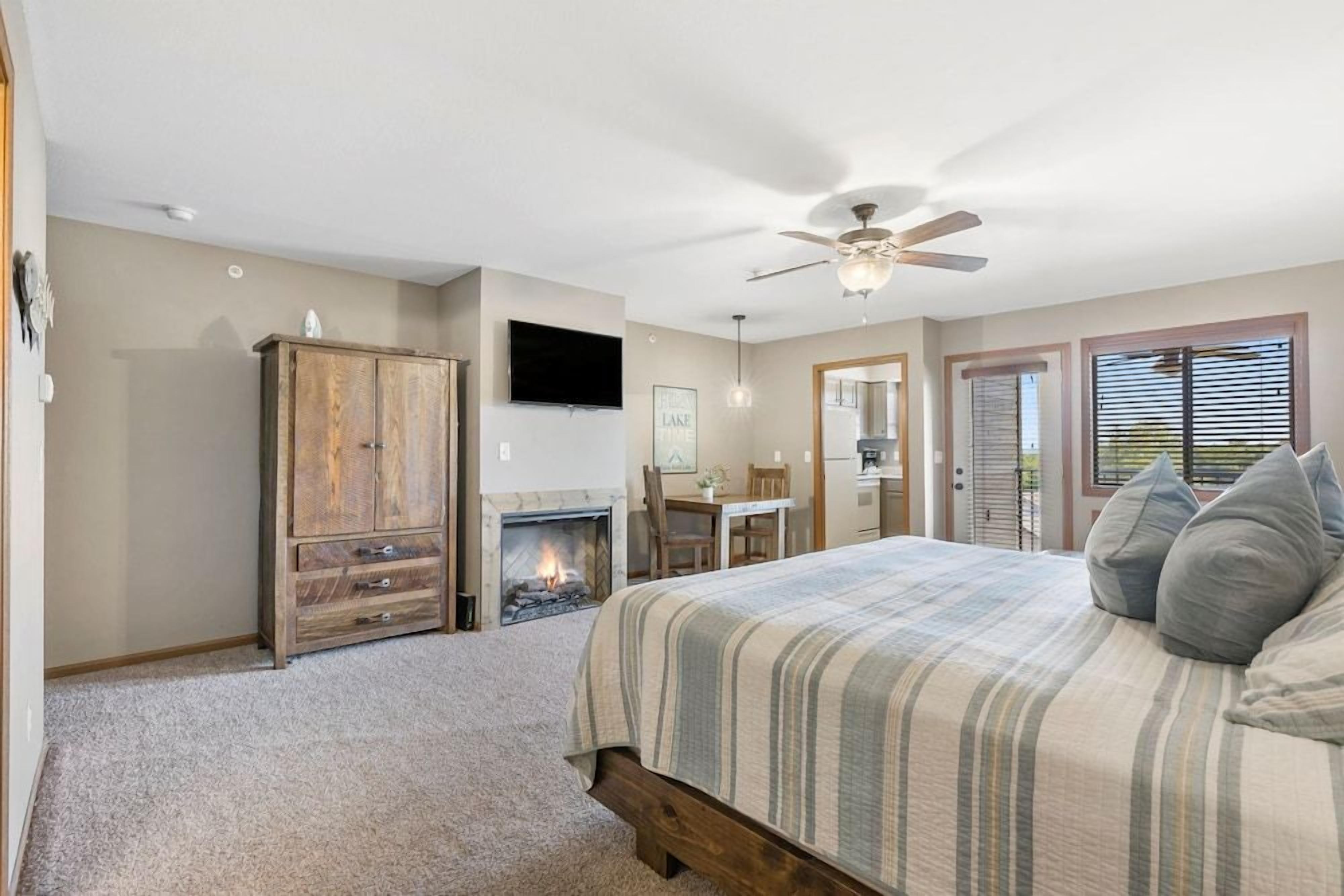 A bedroom with a bed, a wooden cabinet, a fireplace, a ceiling fan, and a television.