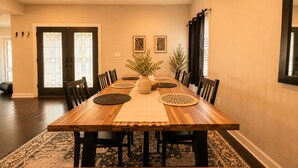 A dining room with a long wooden table, chairs, a vase with plants, and two wall-mounted artworks. - Beautiful bayshore Home Pool,Hot tub,Game room. (Tampa)