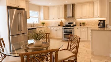 A kitchen with white cabinets, stainless steel appliances, a glass table, wicker chairs, and a tiled backsplash.