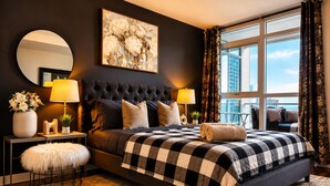 A modern bedroom with a large bed, two bedside tables, a round mirror, and a view of the city. - The Hazelton Horizon Downtown (Toronto)
