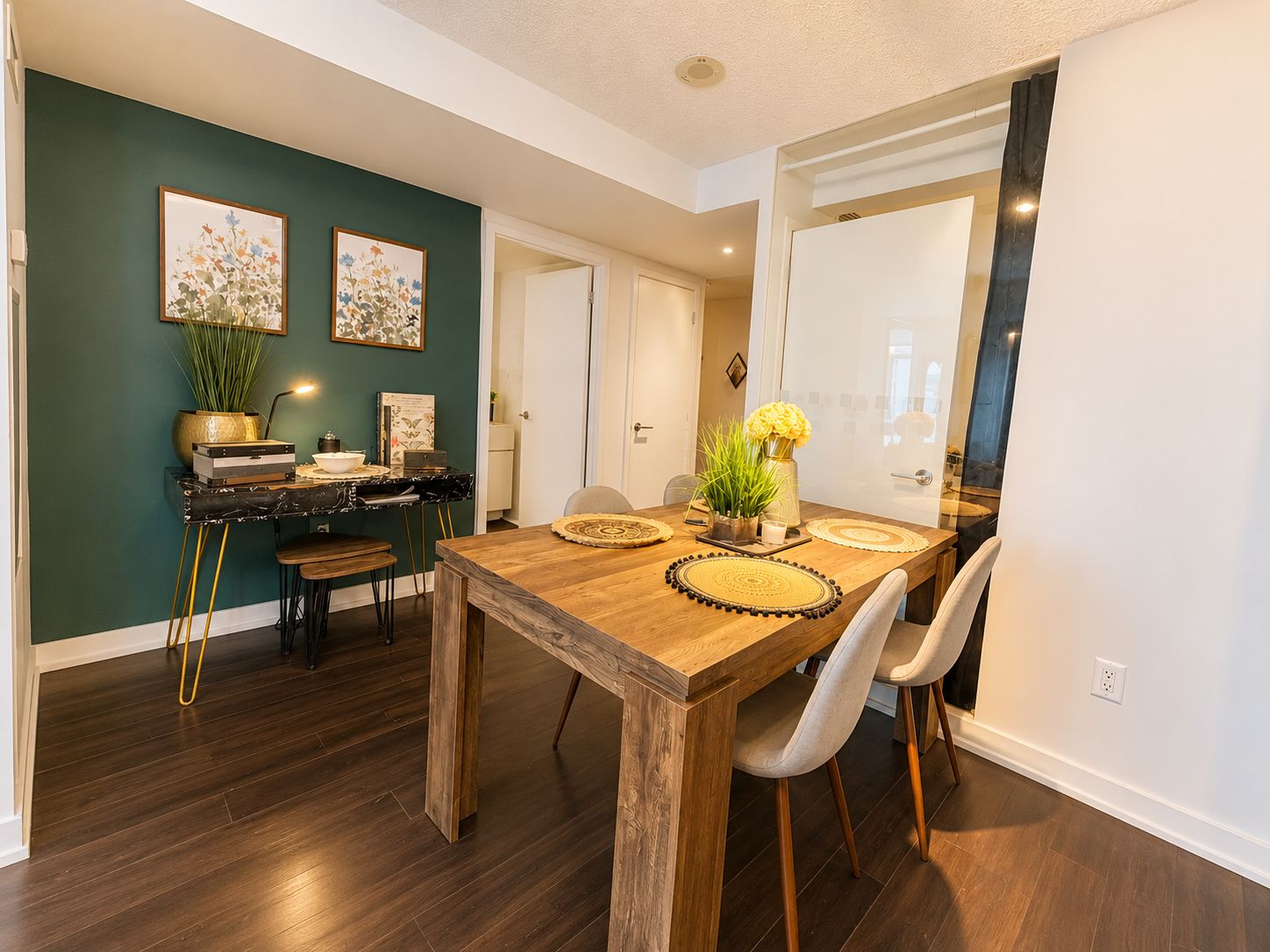 A dining area with a wooden table, chairs, and a dark green wall with floral artwork.