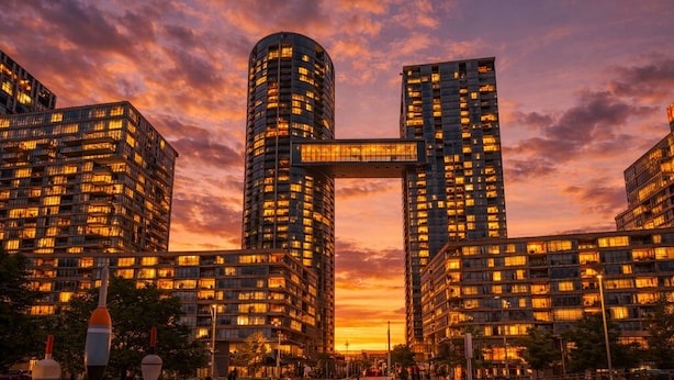 A modern high-rise building with a distinctive cantilevered bridge connecting two towers, surrounded by other high-rise buildings. - The Hazelton Horizon Downtown (Toronto)