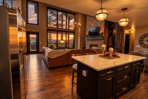 A modern kitchen with a large island, wooden flooring, and a stone fireplace. - Apache Rose | Near Deadwood • ATV/Trailer Parking (Lead)