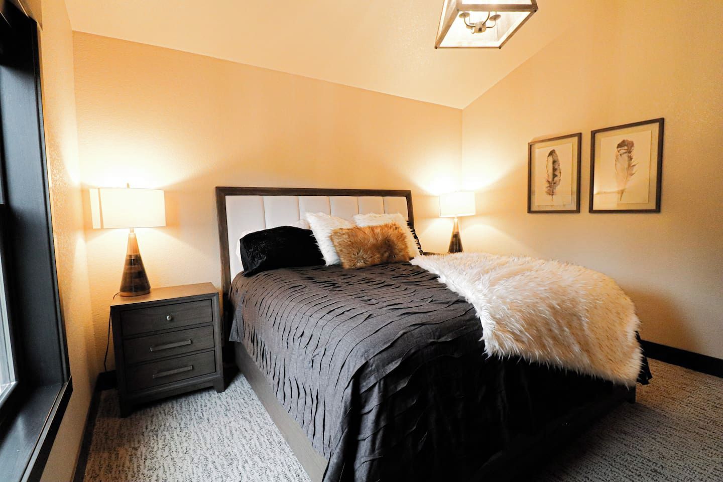 Une chambre à coucher bien rangée, avec un lit, des tables de chevet, des lampes et des œuvres d’art encadrées accrochées au mur.